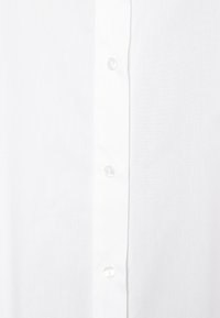 Valkoinen paita, jossa on sileä pinta, keskellä napitus ja kirkkaat muovipainikkeet, pidetään vaaleaa taustaa vasten.