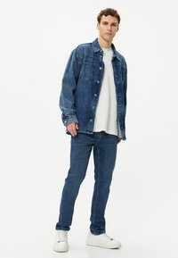 Chaqueta de denim en azul oscuro con botones en la parte delantera y bolsillos en el pecho, combinada con jeans ajustados a juego y zapatillas blancas. Camiseta básica de cuello redondo.