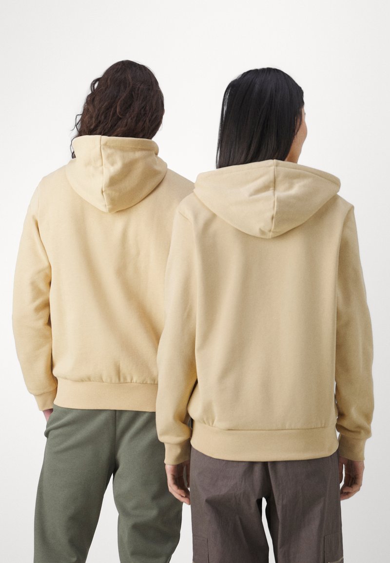 Beige hoodie sweaters van textiel met een gestructureerde stof, voorzien van rib gebreide manchetten en taillebanden, gedragen met respectievelijk groene en bruine broeken.