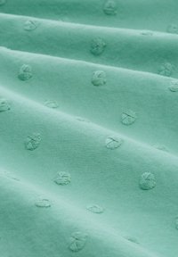 Tela verde menta con sutiles puntos bordados, creando un patrón texturizado. El material parece suave y liso con un ligero brillo.