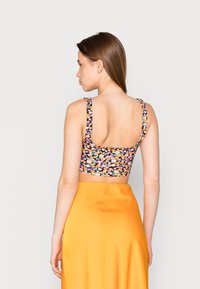 Top cropped preto com flores multicoloridas, alças largas e costas em forma de U, combinado com uma saia laranja. Padrão visível no tecido.