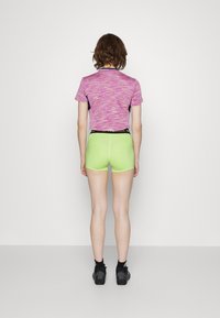 Haut à manches courtes rose vif et violet à motifs associé à un short vert. Une ceinture noire et des chaussures de sport noires complètent le look.