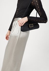 Black leather handbag with a gold rectangular buckle, worn with silver pleated skirt and long-sleeved black lace top.