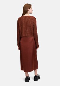 Maglione lavorato a maglia color ruggine con un design cropped abbinato a una lunga gonna in satin marrone scuro, liscia. Scarpe nere con suola spessa completano il look.