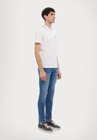 White polo shirt with short sleeves, navy accents on the collar, paired with light blue skinny jeans and grey sneakers.