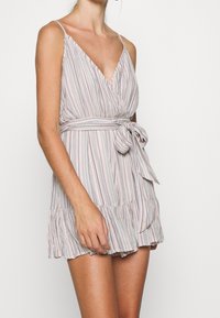 Romper a righe in colori pastello chiari, con scollatura a V, spalline sottili regolabili, vita con laccetto e orlo volant. Realizzato in tessuto leggero.