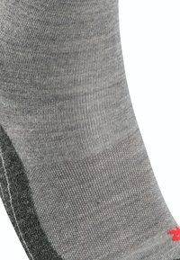 Calcetín gris con textura acanalada y un acento gris más oscuro en el talón; presenta un pequeño logo rojo cerca del puño.