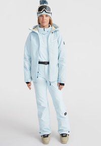 Lichtblauwe waterdichte skijas met een hoge kraag, verstelbare manchetten en ritsdetails, gecombineerd met bijpassende broeken en skischoenen.