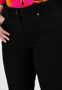 Černé džíny z denimu s hladkým povrchem, vysokým pasem a přední kapsou. Mají stříbrný knoflík a kontrastní prošívání.