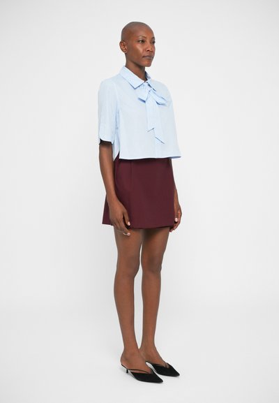 Blauwe gestreepte cropped blouse met een strik, gecombineerd met een bordeauxrode A-lijn rok en zwarte puntige schoenen. Gladde stof, aansluitend ontwerp.