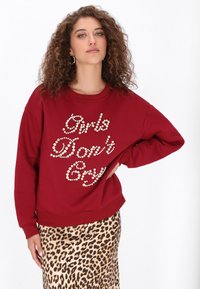 Piros pulóver "Girls Don’t Cry" gyöngyszem díszítéssel, környakkal és bő szabással, leopárdmintás szoknyával párosítva.