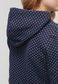 Huvantröja i marinblått tyg med ett mönster av prickar i turkos och rosa. Har en avslappnad passform och en strukturerad yta.