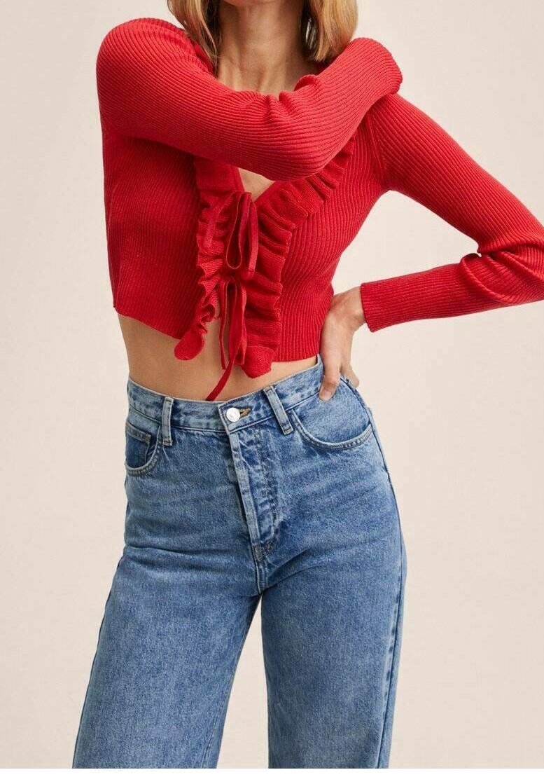 Maglione corto rosso lavorato a maglia con parte anteriore arricciata, dotato di chiusura con fiocco. Abbinato a jeans di denim blu a vita alta, che mostrano una silhouette aderente.
