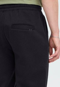 Zwarte sweatpants met een elastische tailleband, voorzien van een achterzak en een gladde textuur. De stof lijkt zacht en casual te zijn.