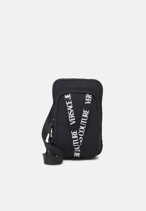 Compacte zwarte crossbodytas met witte "Versace Jeans Couture" logobandjes en een verstelbare schouderriem.