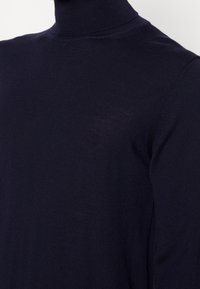 Marinblå polotröja i lätt, strukturerad tyg. Har en åtsittande hals och sömlös axeldesign.