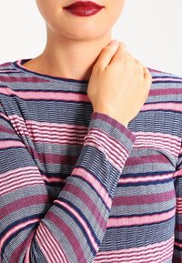 Haut à manches longues avec des rayures horizontales bleu marine, rose et blanc. Tissu texturé avec des largeurs variées créant un intérêt visuel.