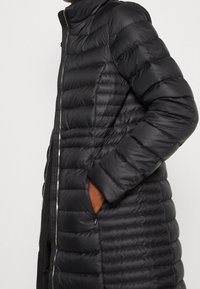 Černý péřový kabát s vysokým límcem, svislým prošíváním a zipovým zapínáním. Obsahuje boční kapsy a elastické manžety.