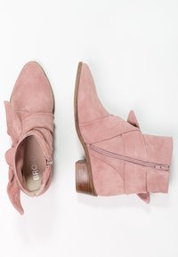 Bottines en daim rose avec un bout pointu, détail de nœud décoratif sur le côté, et fermeture éclair à l'arrière, dotées d'un petit talon en bois.
