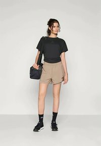 Schwarzes sportliches T-Shirt, beiges Shorts, schwarzer Rucksack; getragen mit schwarzen Socken und Schuhen. Auffälliges Adidas-Logo auf Shirt und Shorts.