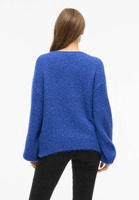 Suéter azul de punto con un corte holgado, hombros caídos y dobladillo acanalado. Textura suave y diseño casual, combinado con pantalones negros.