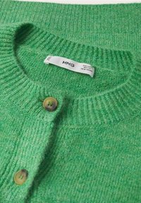 Gros plan d’un cardigan en maille vert avec col côtelé et deux boutons visibles, affichant l’étiquette de la marque MNG à l’intérieur du col.