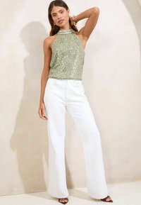 Green sequin halter top paired with white wide-leg pants. The top features a high neck and shimmering texture; pants have a frayed hem.