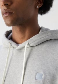 Grijze hoodie met een trekkoord, beschikt over een textuur logo patch op de borst. De stof is zacht met een gladde textuur en een relaxte pasvorm.