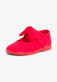 Czerwone dziecięce buty z miękkiego materiału, z zaokrąglonym noskiem i wyraźnym detalem w postaci węzła z przodu. Wyposażone w zapięcie na rzepy, co ułatwia zakładanie.