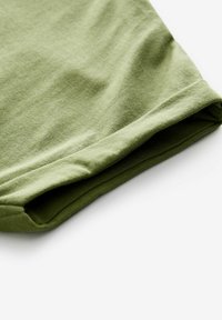 Olive roheline puuvillane kangas, millel on sile tekstuur, volditud ääres, näidates lihtsat disaini ja puhtaid servi.