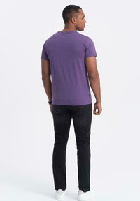 Lila bomullströja med rund hals, korta ärmar och en avslappnad passform, kombinerad med svarta jeans och vita sneakers.