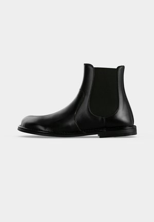 Botte Chelsea en cuir noir avec panneau latéral élastique et talon bas, affichée de profil sur un fond clair uni.