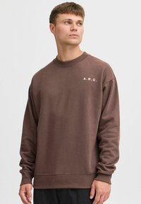 Brun sweatshirt med rund halsudskæring, ribbede manchetter og kant. Har hvid "A.R.C." tekst på venstre bryst. Blødt, struktureret stof.