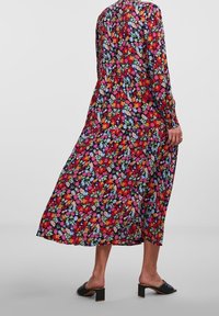 Pitkähihaiset kukkakuvioiset mekko, jonka liehuva helma punaisissa, vaaleanpunaisissa, sinisissä ja vihreissä sävyissä. Mekossa on kerroksittainen muotoilu ja napitus selän takana.