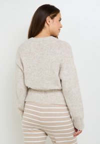 Maglione beige a maglia con vestibilità comoda, orlo a coste e finitura testurizzata. Abbinato a pantaloni chiari a righe in toni neutri.
