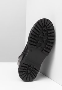 Botte en cuir noir avec une semelle en caoutchouc texturée. Elle présente un motif de bande de roulement robuste et une fermeture éclair latérale pour un enfilage facile.