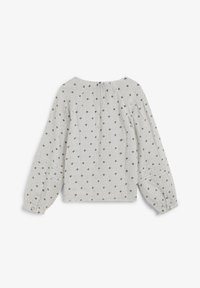 Blusa blanca con un patrón de puntos en gris, mangas largas abullonadas y puños abotonados. Tejido de textura suave con cuello redondeado.