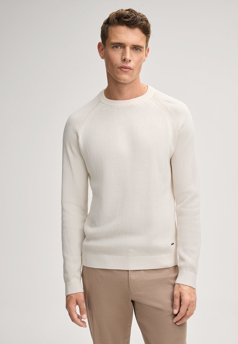 Hellbeige gestrickter Pullover mit strukturiertem Muster, gerippten Bündchen und Saum, Rundhalsausschnitt, kombiniert mit hellbraunen Hosen.