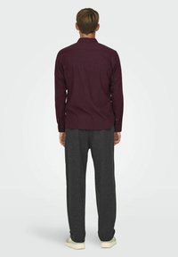 Bordeaux knap-up skjorte med lange ærmer og rygbærestykke, parret med mørkegrå sweatpants og lyse sneakers. Glat stofoverflade.