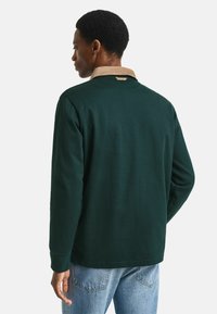 Camicia a maniche lunghe verde scuro con colletto in corduroy a contrasto. Materiale in cotone morbido, design semplice e vestibilità comoda. Etichetta del marchio discreta sul retro.