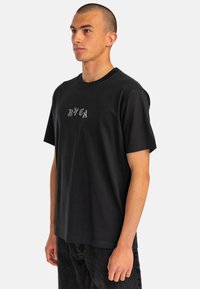 Black cotton t-shirt with a crew neckline, short sleeves, and a small gray logo print on the chest, styled with dark jeans.