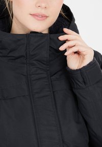 Sort jakke med høj krave, tekstureret foer og synlige syninger. Stoffet ser glat og let blankt ud.