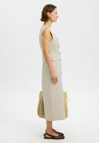 Lys beige linnedress med ærmeløst design, frontknapper og sidelommer. Parret med brune perforerede flade sandaler og en vævet taske.