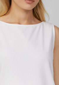 Top blanco sin mangas con un amplio escote barco, hecho de una suave tela de algodón. Textura lisa sin patrones ni acentos visibles.