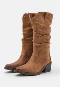 Botas de vaquero de imitación de cuero marrón con un diseño holgado, punta puntiaguda y tacón apilado. Presentan detalles de costura alrededor de la parte superior.