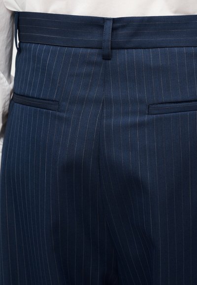 Παντελόνι σε σκούρο μπλε χρώμα με λεπτές κάθετες ρίγες, με ομαλή υφή υφάσματος, διαθέτει δύο πίσω τσέπες και εφαρμοστή γραμμή. Η μέση είναι δομημένη και καθαρή.