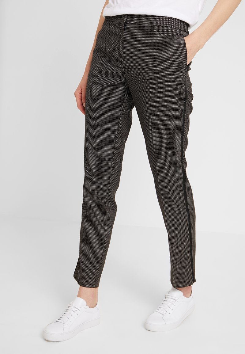Pantalons à rayures noir et blanc avec une coupe slim, jambes droites, poches latérales et une texture lisse, associés à des baskets blanches.