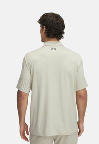 Polohemd in hellbeige mit strukturiertem Stoff, kurzen Ärmeln und einem Kragen. Auf der Rückseite befindet sich ein kleines schwarzes Logo.
