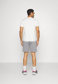 Hvit trenings t-skjorte og grå shorts, med rund hals og korte ermer. Brukt med hvite sokker og joggesko med rosa detaljer.