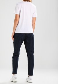 Camisa de tirantes corta blanca combinada con pantalones a rayas navy y zapatillas blancas. La camiseta es sencilla y ajustada, mientras que los pantalones tienen un aspecto a medida.